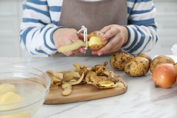 Woman peeling fresh potato at white marble table, closeup