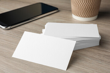 Blank business cards and smartphone on wooden table, closeup. Mockup for design