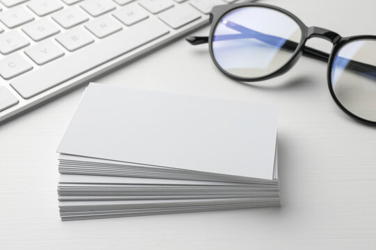Blank business cards, glasses and keyboard on white table, closeup. Mockup for design