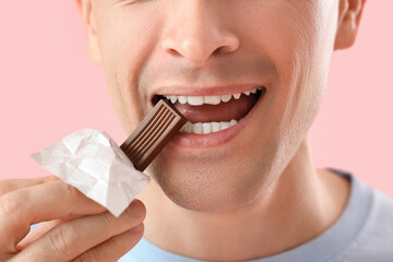 Handsome man eating chocolate on pink background, closeup