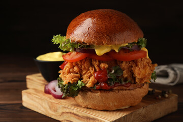 Delicious burger with crispy chicken patty on wooden table, closeup