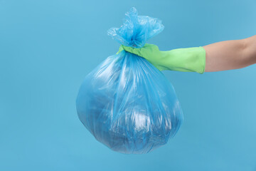 Woman holding plastic bag full of garbage on light blue background, closeup