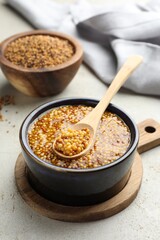 Whole grain mustard in bowl and spoon on light table