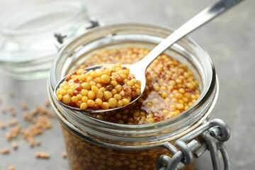 Whole grain mustard in jar and spoon on table, closeup