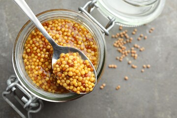 Whole grain mustard in jar and spoon on grey table, top view. Space for text