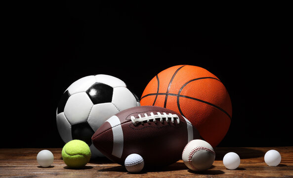 Many different sport balls on wooden table against black background