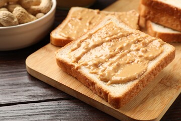 Delicious toasts with peanut butter on dark wooden table, closeup