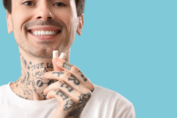 Young tattooed man with chewing gum on blue background, closeup