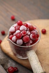 Frozen red cranberries in glass pot on wooden table, closeup