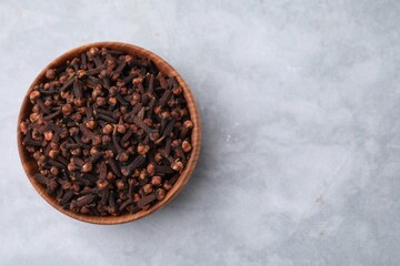 Aromatic cloves in bowl on gray table, top view. Space for text