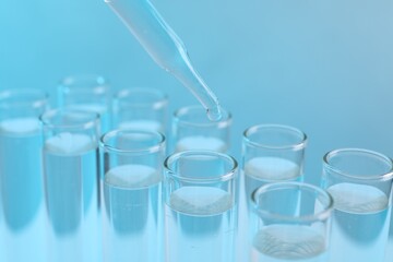 Laboratory analysis. Dripping reagent into test tube on light blue background, closeup