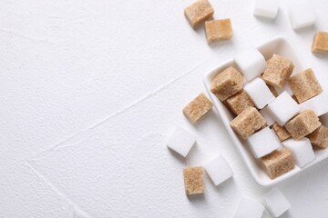 Different sugar cubes in bowl on white table, top view. Space for text