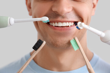 Handsome young man with different toothbrushes on grey background. Dental care concept