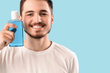 Handsome young man with bottle of mouthwash on blue background. Dental care concept