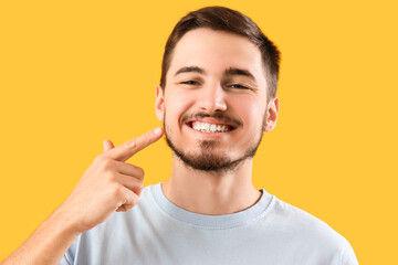 Handsome young man pointing at healthy teeth on yellow background. Dental care concept