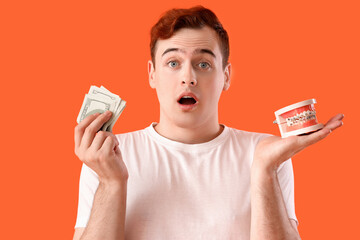 Young man holding jaw model with braces and money on orange background