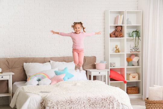 Cute little girl jumping on bed in bedroom