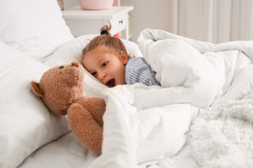 Cute little girl with toy bear lying in bed