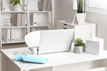 Doctor's workplace with laptop, hot water bottle and pills in medical office