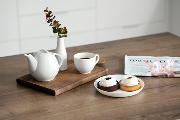 Modern breakfast setup with coffee, fresh pastries and newspaper on wooden table in kitchen