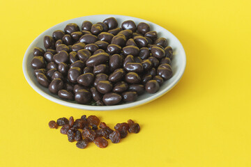 Dried raisins with dark chocolate in a bowl on a yellow background