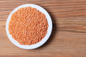 A pile of split red lentils on a white plate on a pine surface