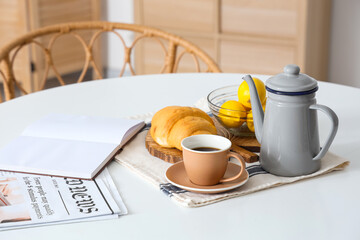 Dining table with cup of coffee, open book and croissant in light room