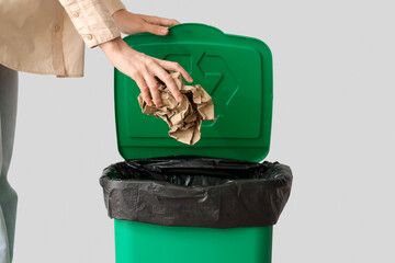 Woman throwing crumpled paper into trash bin near grey wall, closeup