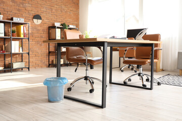 Empty trash bin near table in interior of modern office