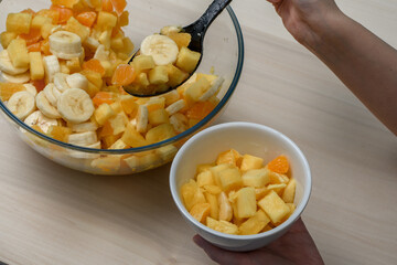 Nakładać porcję sałatki owocowej z bananem, pomarancza, brzoskwinia i ananasem do miseczki - obrazy, fototapety, plakaty