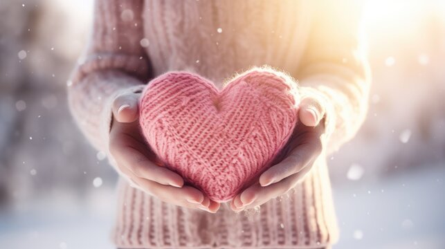 Close-up of a woman holding a knitted pink heart in her hands, a defocused blurred background with snowflakes. Valentine's Day greeting card. Feelings and emotions.