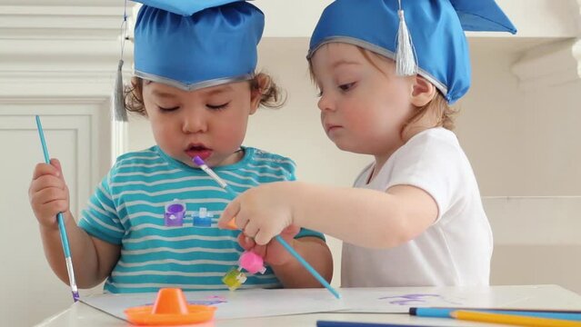 Two cute babies boy and girl in blue graduation hats paint colors