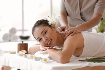 Obraz na płótnie Canvas Young Asian woman with flower getting massage in spa salon, closeup