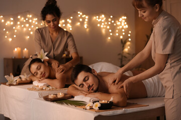 Young couple getting massage from therapists in dark spa salon