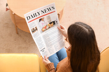 Young woman reading newspaper on sofa at home, top view