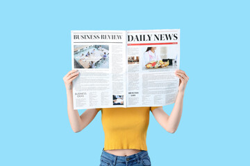 Young woman reading newspaper on blue background - obrazy, fototapety, plakaty