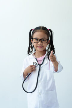 A girl wearing a doctor's uniform, standing with smiling glasses and a stethoscope is playing a doctor. and give a thumbs up showing excellent work, excellent, on a white background.
