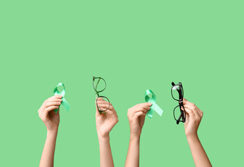 Female hands with ribbons and eyeglasses on green background. Glaucoma awareness concept