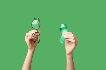 Female hands with ribbon and eyeglasses on green background. Glaucoma awareness concept