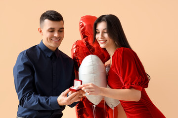 Young man with heart-shaped balloons proposing to his girlfriend on beige background. Valentine's Day celebration