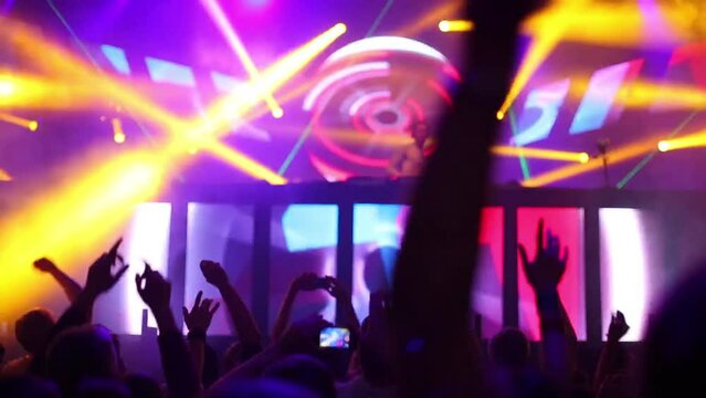 Hands of dancing people with phones and DJ on stage in nightclub