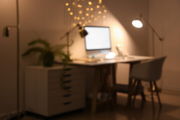 Blurred view of office with workplace and glowing lamps at night