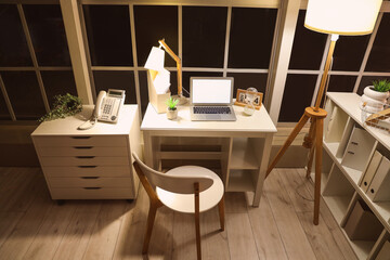Workplace with blank laptop and glowing lamp in modern office at night
