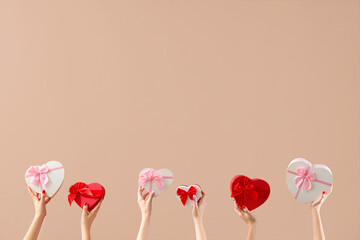 Female hands holding heart-shaped gift boxes on beige background. Valentine's Day celebration