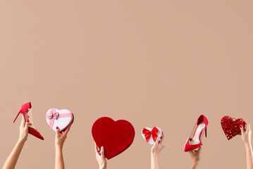 Female hands holding heart-shaped gift boxes and high heeled shoes on beige background. Valentine's...