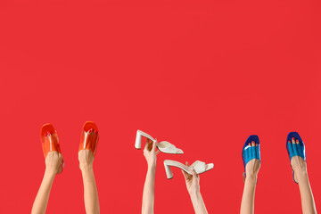 Female hands holding different shoes on red background - obrazy, fototapety, plakaty