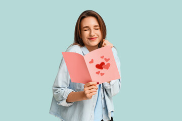 Beautiful young woman holding greeting card with hearts on blue background. Valentine's Day...