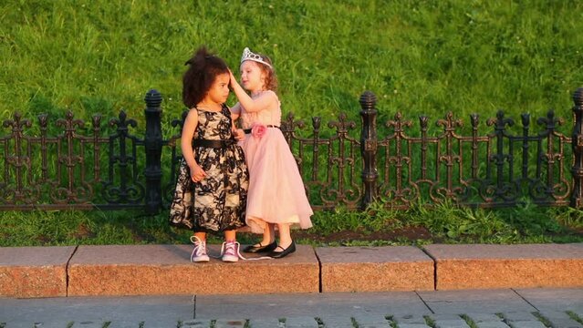 Girls stand on curb next to forged fence and correct hairstyle