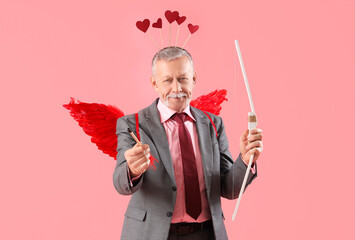 Mature man dressed as Cupid with bow and arrow on pink background. Valentine's Day celebration