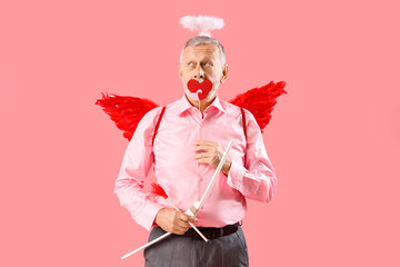 Mature man dressed as Cupid with hearts and bow on pink background. Valentine's Day celebration
